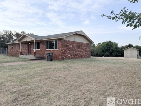 A house with a brown brick exterior and a white roof is surrounded by a grassy area.