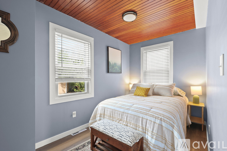 A bedroom with a bed, a window with blinds, a nightstand with a lamp, and a picture on the wall.