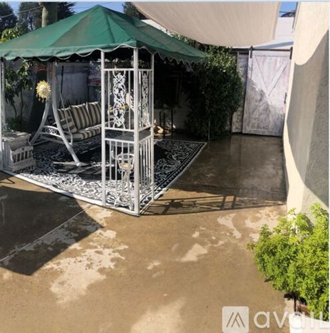 A white metal gazebo with a green canopy is situated on a concrete patio.