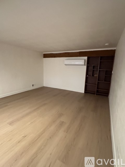 A room with wooden flooring and a white wall with a shelf.