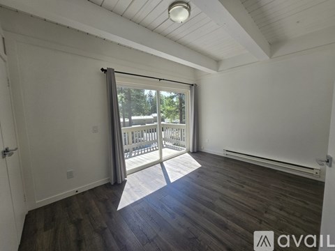 A room with wooden floors and a sliding glass door leading to a balcony.