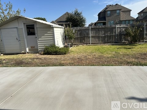 A small white shed sits in a grassy area next to a paved road.