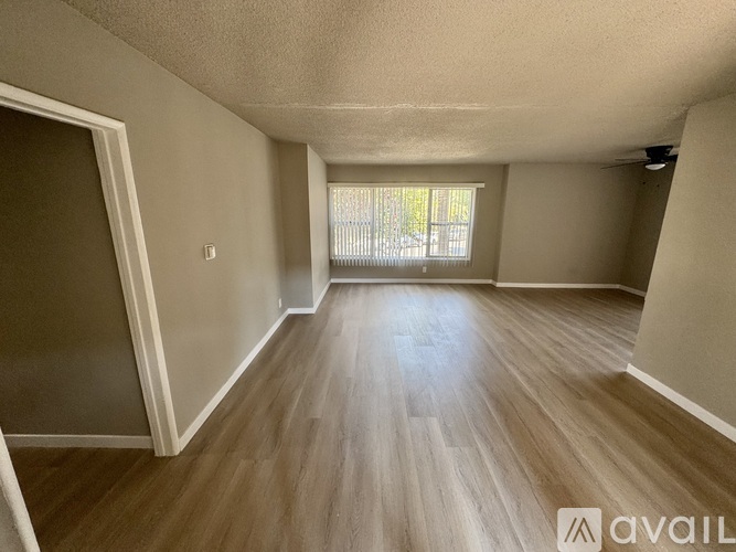 A spacious room with wooden flooring and a window with blinds.