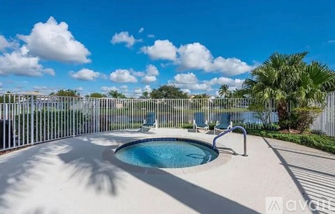 A pool surrounded by a white fence with a blue sky and clouds in the background.