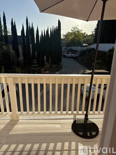 A balcony with a white railing and a view of a street with cars and trees.