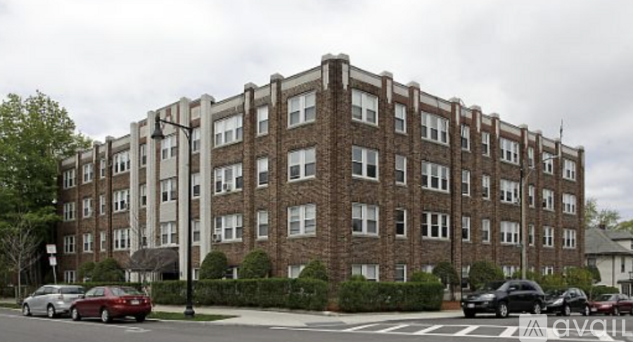 A large brick building with many windows is in front of a street with cars.