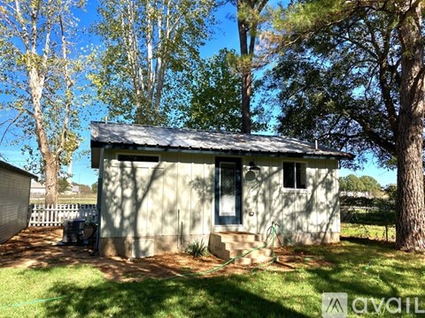 A small house with a metal roof is surrounded by trees and grass.