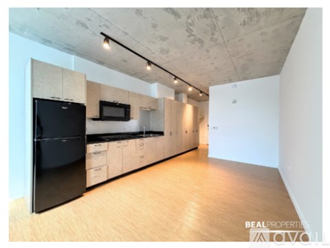 A kitchen with a black fridge and microwave, wooden floors, and white walls.