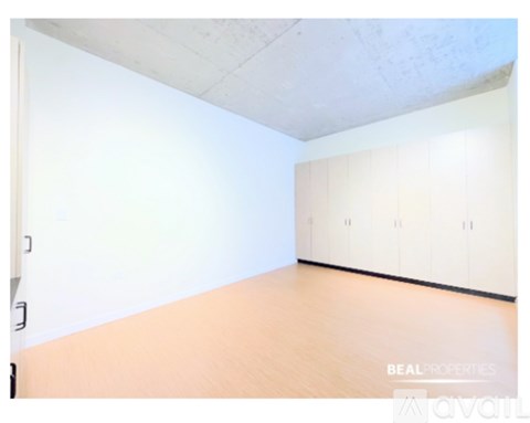 A room with wooden flooring and white walls, with a row of cabinets on the wall.