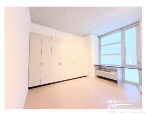 A room with a white wall, a window, and a set of white cupboards.