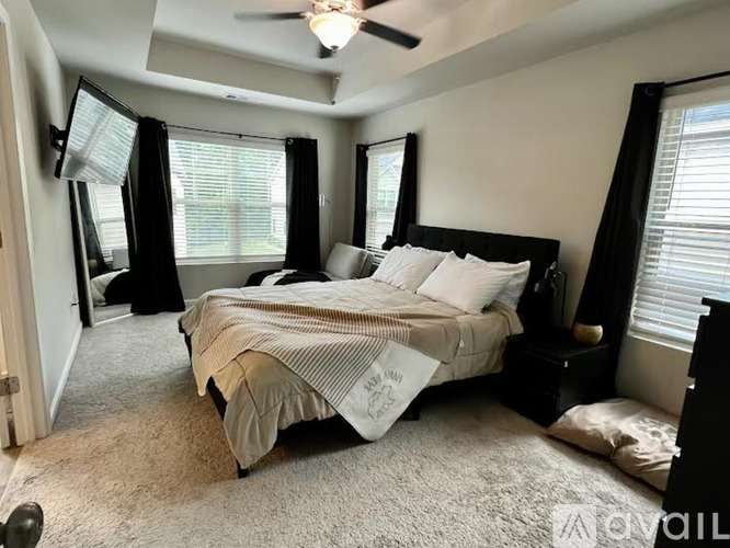 A bedroom with a bed, a ceiling fan, and a window with black curtains.