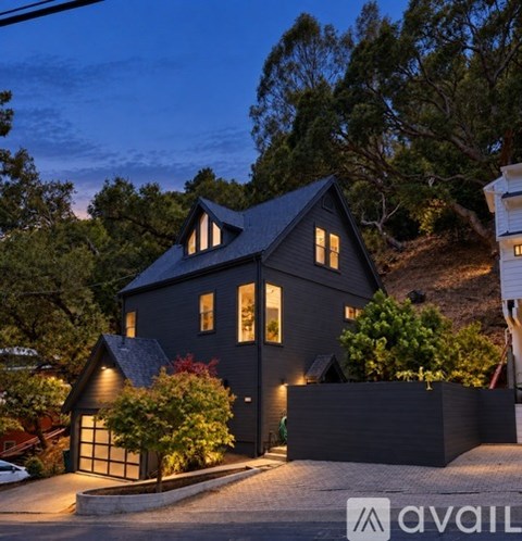 A house with a dark grey exterior and a black roof is surrounded by trees and bushes.