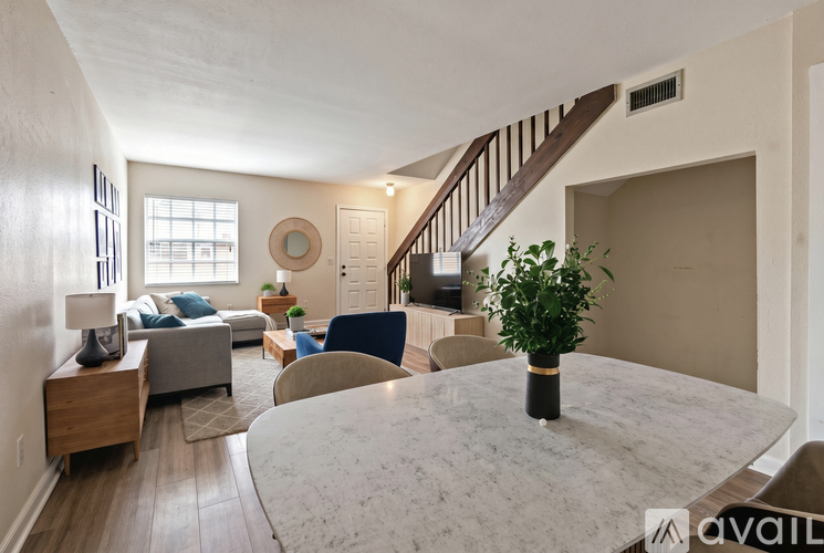 A living room with a grey sofa, a round mirror, a wooden table, and a staircase.