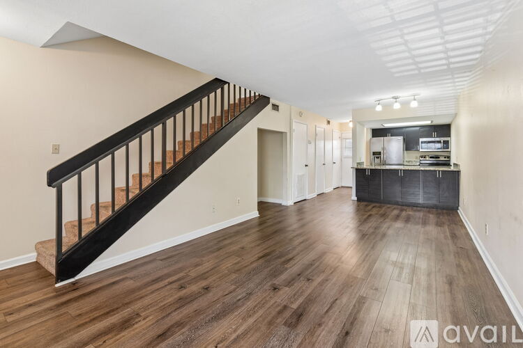 A spacious room with wooden floors and a staircase with black railings.