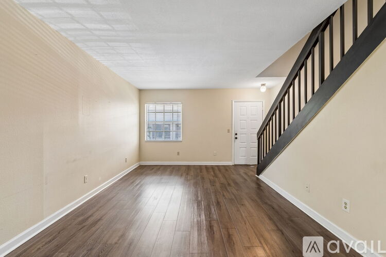 A spacious room with wooden floors and a staircase on the right side.