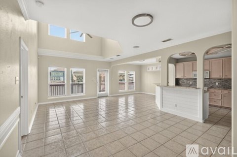 A spacious living room with a kitchen area in the background.
