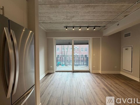 A kitchen with a refrigerator on the left and a view of a balcony through the sliding glass door.