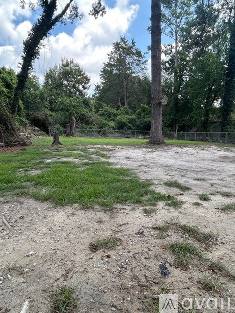 A dirt field with a fence and trees in the background.