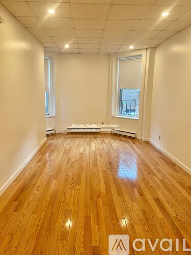 A room with wooden floors and white walls, with a window showing a cityscape.