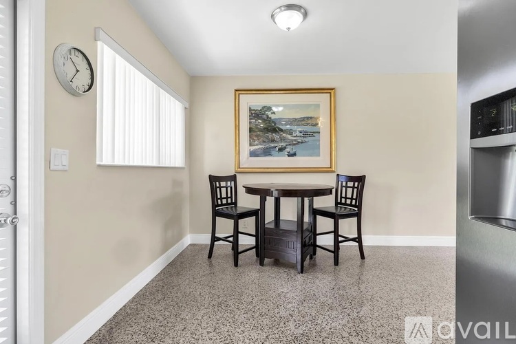 A dining room with a table and chairs and a painting on the wall.