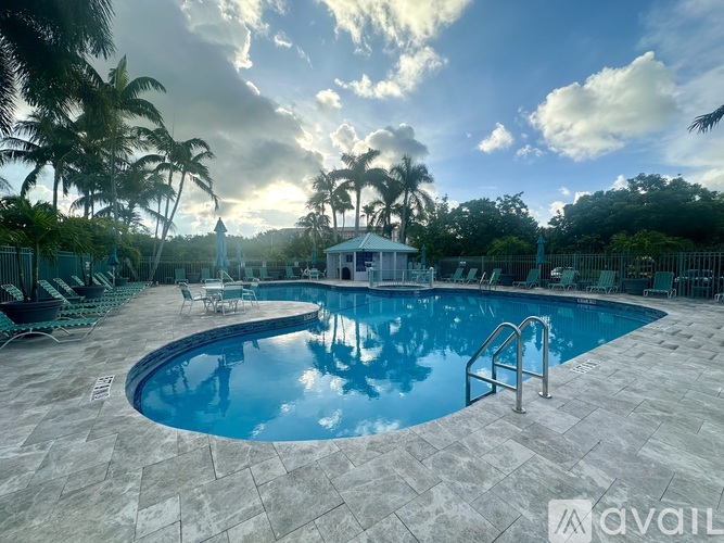 A swimming pool surrounded by palm trees and a white gazebo.