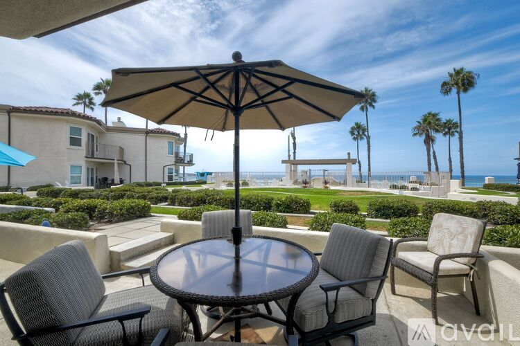 A patio with a table, chairs, and an umbrella overlooking the ocean.