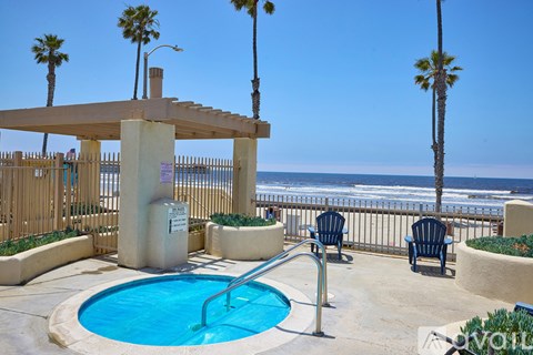 A pool area with a hot tub and chairs overlooking the ocean.