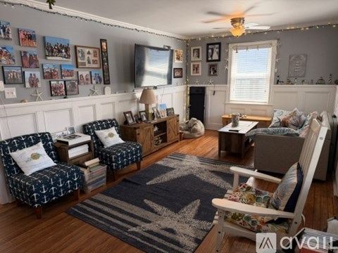 A living room with a white couch, a chair with a blue and white pattern, a rug with a star design, and a television mounted on the wall.