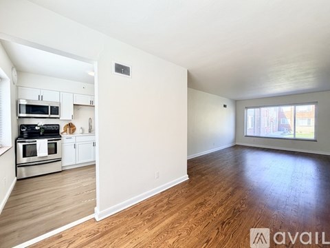 A spacious living room with hardwood floors and a kitchen area with stainless steel appliances.