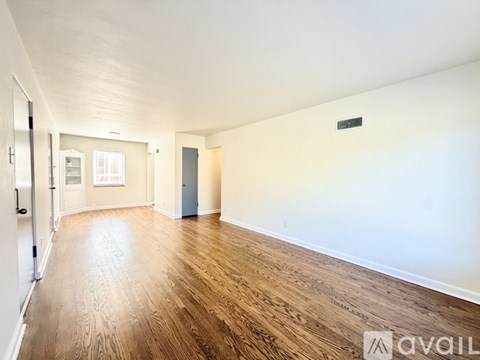 A spacious room with wooden flooring and white walls.