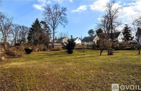 A grassy field with trees and houses in the background.