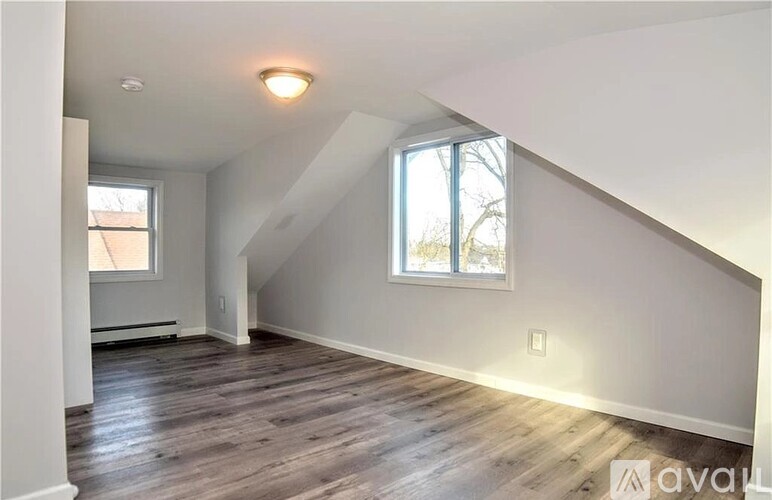 A spacious attic room with wooden flooring and a window.