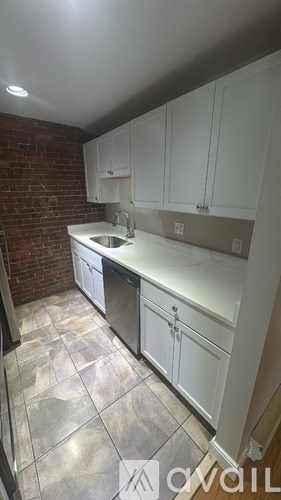 A kitchen with white cabinets and a brick wall.