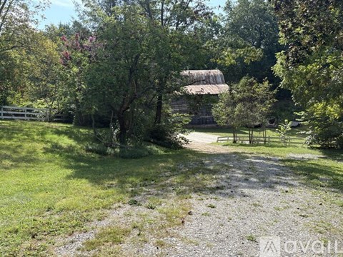 A gravel path leads to a wooden fence and a building in a lush green area.