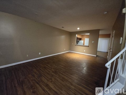 A spacious room with wooden flooring and a staircase on the right side.