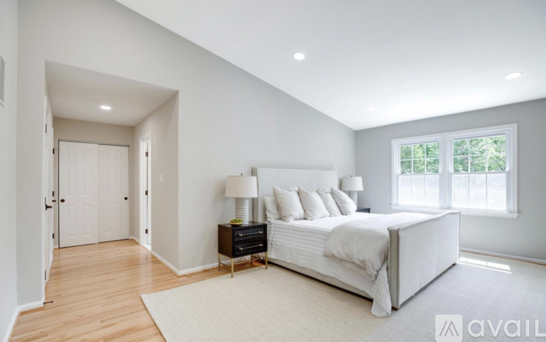 A bedroom with a large bed, a nightstand with a lamp, and a window with a view of trees.