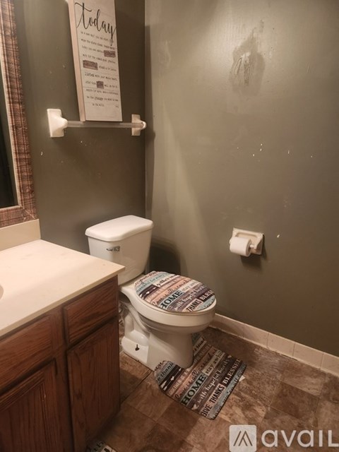 A toilet with a newspaper print toilet paper is in a bathroom.
