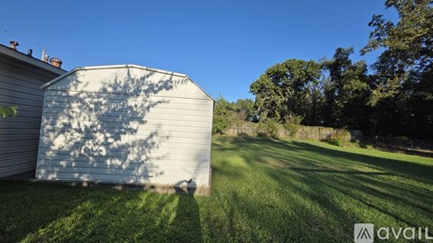 A shed sits in a grassy field with trees in the background.