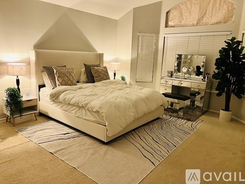 A bedroom with a large bed, a desk with a mirror, and a plant.