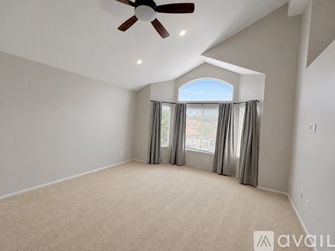 A spacious room with a ceiling fan and a large window with curtains.