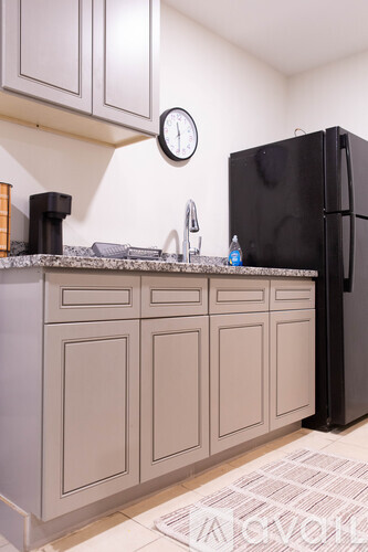 A black refrigerator sits next to a counter with a clock on the wall.