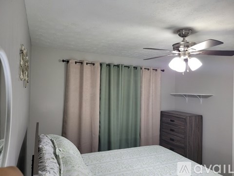 A bedroom with a bed, dresser, and a ceiling fan.