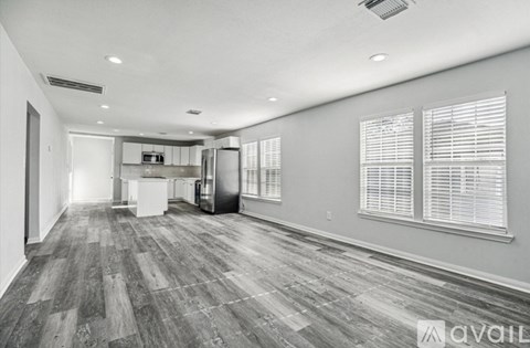 A spacious room with wooden flooring and a kitchen area in the background.