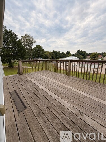 A wooden deck with a white railing and a view of trees and a white tent in the distance.