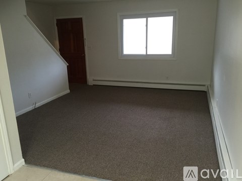 A room with a carpeted floor, a window, and a door.