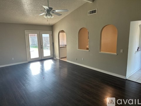 A spacious room with a ceiling fan and arched windows.