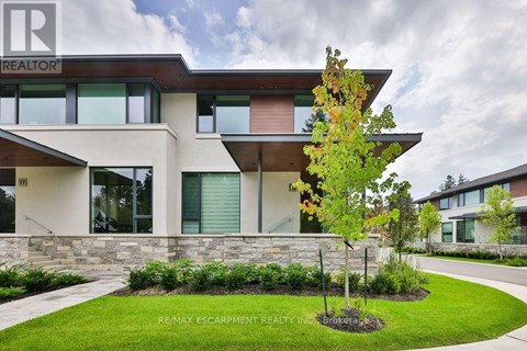 A modern house with a stone wall and a tree in front.