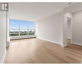 A spacious room with wooden flooring and a large window overlooking a landscape.