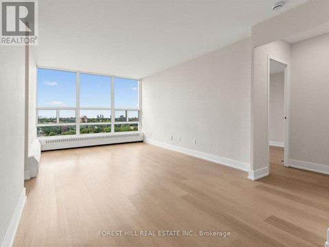 A spacious room with wooden flooring and a large window overlooking a landscape.