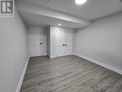 A room with wooden flooring and white walls, with two doors and a ceiling light.